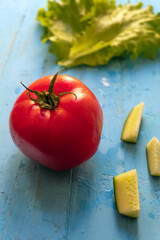 Pink tomato, three cucumber slices and green salad leaves on a blue background