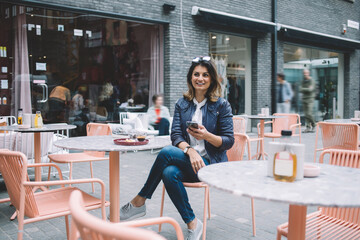 Smiling woman with smartphone and coffee in street cafe
