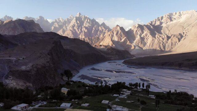 Aerial view of the Hussaini village, with its green fields, houses and dry Hunza river, facing the peaks of Passu Cones in the background, beautiful travel destination in Pakistan