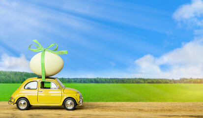 Retro car carrying an easter egg on the roof on green field and blue sky landscape background.