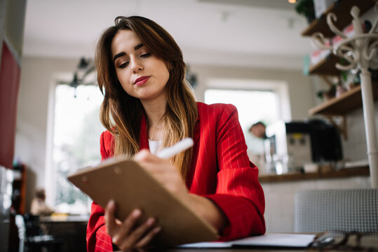 Young woman writing information in notepad