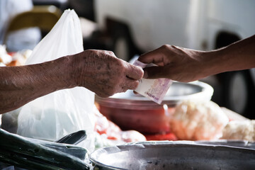 Mãos de pessoas em feira fazendo pagamento com notas de dinheiro.