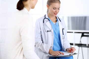 Doctor and patient during consultation. Physician at work filling up medication history record while sitting in emergency hospital, portrait shoot. Medicine and health care concept