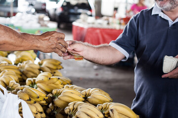 Mãos de pessoas fazendo pagamento em feira. Banca de bananas.