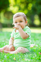 Cute kid in a green bodysuit sitting on the grass in summer plays with developing toys. The baby gnaws silicone cubes. Child development up to one year