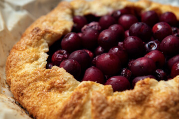 Galette with ripe red cherry on dark blue background. Homemade sweet open pie. Close-up.