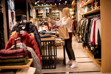 Young woman shopping and searching among clothes at clothes store