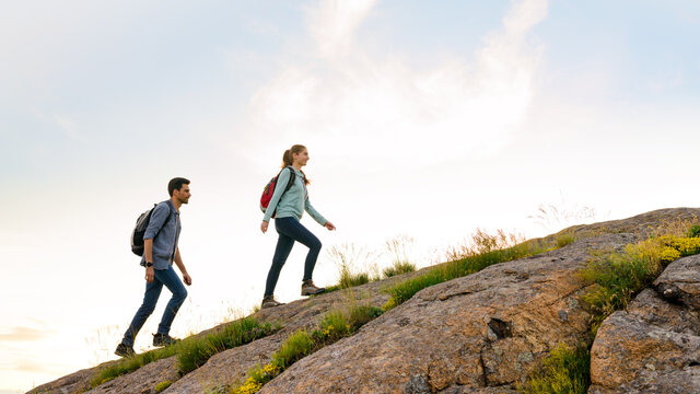 Couple of Young Happy Travelers Hiking with Backpacks on the Rocky Trail at the Evening. Family Travel and Adventure