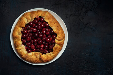 Galette with ripe red cherry filling on dark blue background. Homemade sweet open pie. Space for text. Top view.