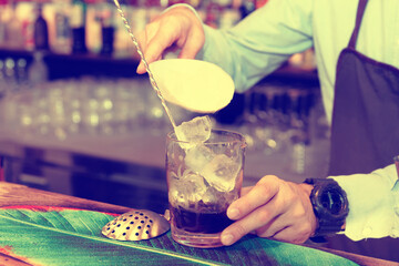 Bartender is adding ice cubes to mixing glass, toned