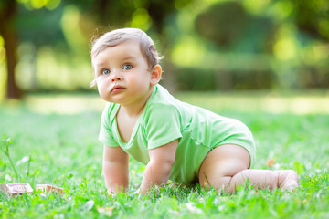 Cute toddler in green bodysuit crawls on the grass in the summer. The baby learns to crawl on the grass.