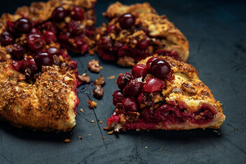 A piece of galette with ripe red cherry filling. Homemade sweet open pie on dark textured backdrop.