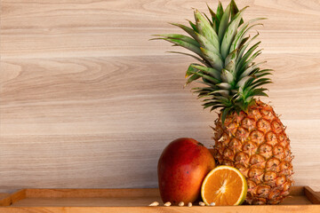 Mango, orange, with pineapple on wooden background