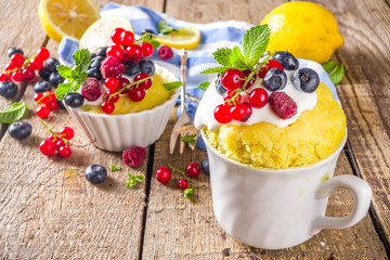 Lemon Mug Cake. Summer sweet dessert in  Microwave. Lemon Mug Pies with fresh berries and whipped cream, on wooden background