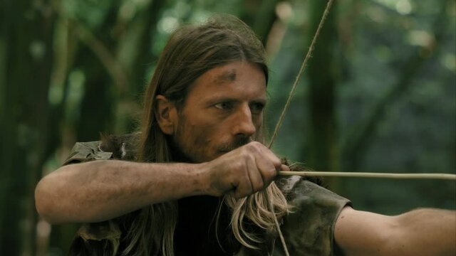 Long-Haired Caveman Takes Aim Carefully Then Fires Bow And Arrow