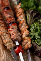 BBQ Healthy barbecued lean cubed pork and chicken kebab on skewers with vegetables, fresh lettuce and tomato salad, close up view on a dark background. Food for a picnic.
