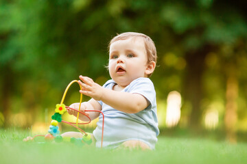 Healthy toddler plays with developing toy sitting on summer grass