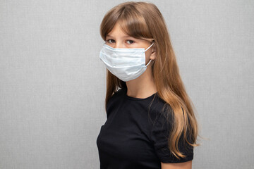 Sad little girl in a black t-shirt and a medical mask. Coronavirus concept, COVID-19.