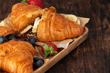Half cut croissant decorated with fresh berries on wooden table