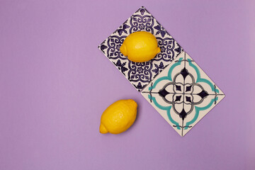 Ceramic tiles with ornament on a purple background and juicy lemons, top view