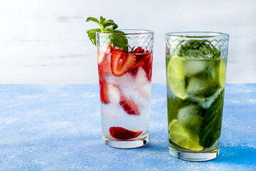 Two glass of refreshing cool detox drink with strawberry, lime and mint on blue background. Various summer lemonades or ice tea. Mojito cocktail with ice cubes. Healthy eating. Сopy space for text