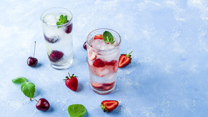 Two glass of refreshing cool detox drink with strawberry, cherry and mint on blue background. Various summer lemonades or ice tea. Mojito cocktails with ice cubes. Healthy eating. Сopy space for text