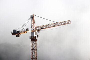 Construction crane in a fog on background of mist sky. Housing construction, real estate business