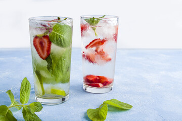 Two glass of refreshing cool detox drink with strawberry, lime and mint on blue background. Various summer lemonades or ice tea. Mojito cocktail with ice cubes. Healthy eating. Сopy space for text