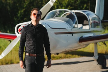 Young handsome businessman is standing near private plane. Confident and successful man in airport.