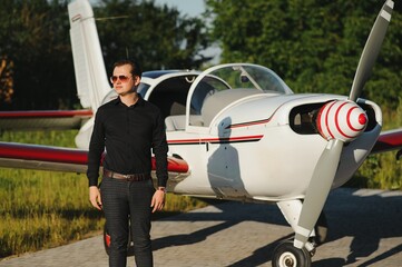 Young handsome businessman is standing near private plane. Confident and successful man in airport.