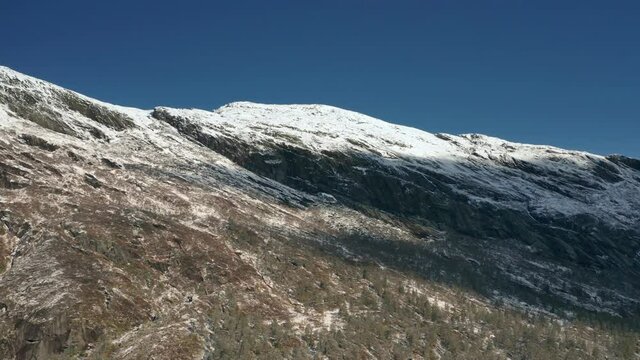 Aerial view of the harsh northern landscape. Dense pine forest covering rocky foothills, fresh snow covering mountain tops. Dark blue clear sky above.