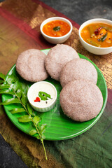 Ragi Idly, finger millet Idli, Sambar, coconut chutney healthy home made breakfast dish Kerala, Karnataka, India. steam cooked finger millet batter. Top view South Indian food dark black background.