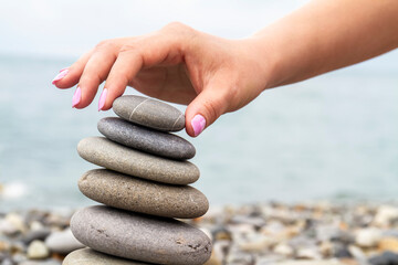 Girl builds a pyramid of sea stones on the seashore at the pebble beach. Concept of harmony and...