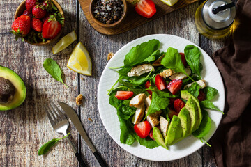 Lunch for keto. Summer salad with strawberries, grilled chicken and avocado on a rustic table. Top view flat lay background.