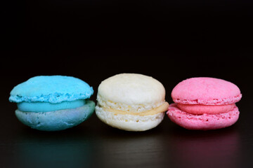 Three sweet macarons, in the colors of the French flag, lie side by side against a dark background