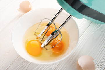 Mixer whisk immersed in a bowl with broken eggs