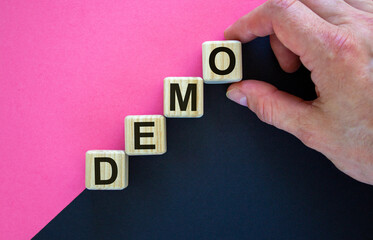 Wood cubes with word 'demo' stacking as step stair on paper black and pink background, copy space. Business concept.