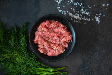 Homemade minced meat in a black bowl with ingredients. Fresh Raw mince. Top view with copy space