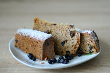 beautiful cake with raisins cut into three pieces sprinkled with powdered sugar on top. Also on the plate are blueberries