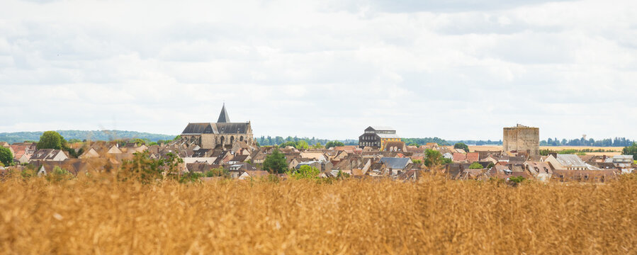 Panoramic view of medieval town Houdan with its ancient church and fortified tower through the blurry field.  Ile-de-France, France. French countryside tourism background banner.