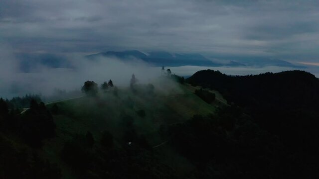 Jamnik, Slovenia - 4K aerial drone footage of flying towards St.Primoz church on a dark and foggy summer morning