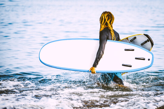 Attractive Blonde hipster surfer with dreadlocks looking at the sea holding cool surfboard. Back to surf, Outdoors sports adventure lifestyle 