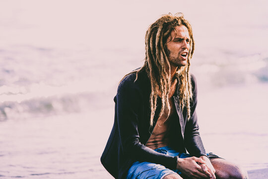 Attractive Blonde hipster surfer with dreadlocks looking at the sea holding cool surfboard. Back to surf, Outdoors sports adventure lifestyle 