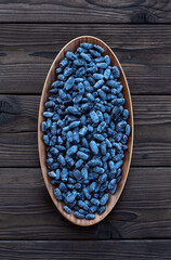 Honeysuckle in an oval wooden dish on a dark wooden background. Fresh harvest of honeysuckle berries from the garden.