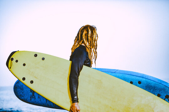 Attractive Blonde hipster surfer with dreadlocks looking at the sea holding cool surfboard. Back to surf, Outdoors sports adventure lifestyle 