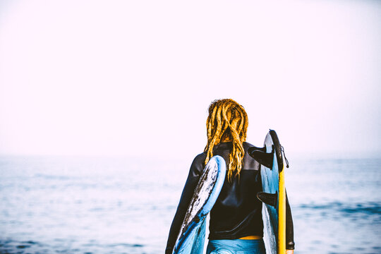 Attractive Blonde hipster surfer with dreadlocks looking at the sea holding cool surfboard. Back to surf, Outdoors sports adventure lifestyle 