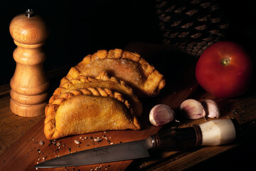 delicious Argentine empanada on wooden board, with knife, garlic and pepper shaker