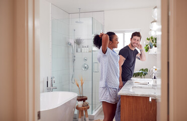 Couple Wearing Pyjamas Standing In Bathroom At Sink Getting Ready In The Morning