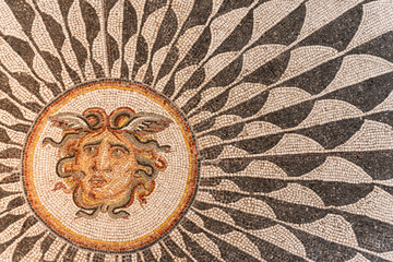 Colorful ancient mosaic illustration showing a medusa´s head inside a symbolic sun