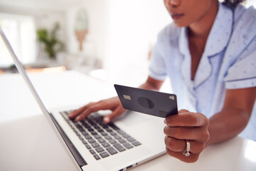 Close Up Of Woman Wearing Pyjamas In Kitchen Making Online Credit Card Purchase On Laptop